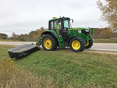 A maintenance crew member mowing the ditch along a state highway.